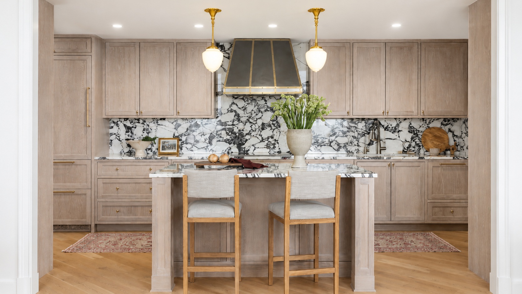 White oak kitchen with brass hardware, full-height marble slab backsplash, and custom steel-and-brass range hood