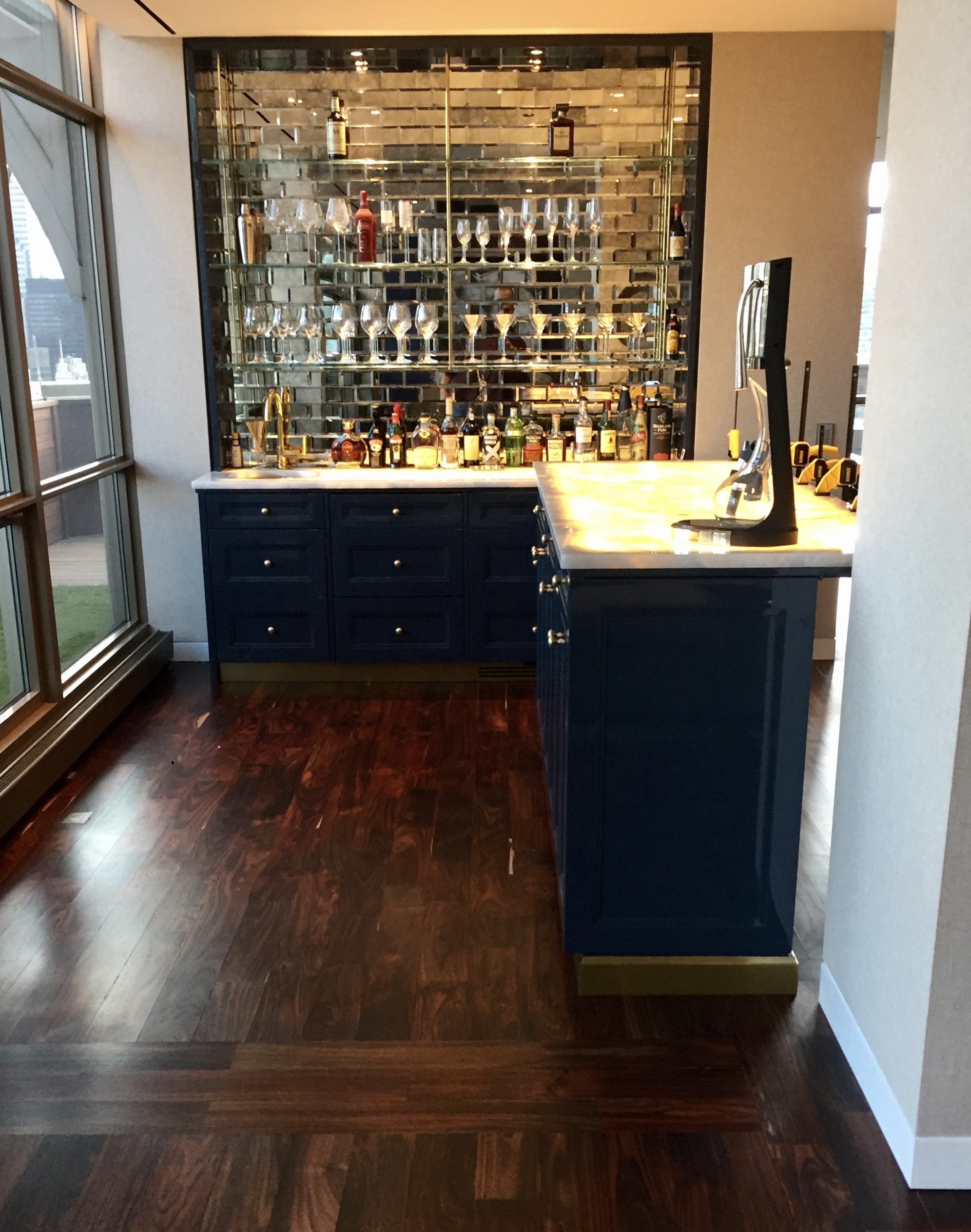 Navy home bar with antique brass hardware, mirrored subway tile backsplash, marble countertop, and keg tap on the peninsula