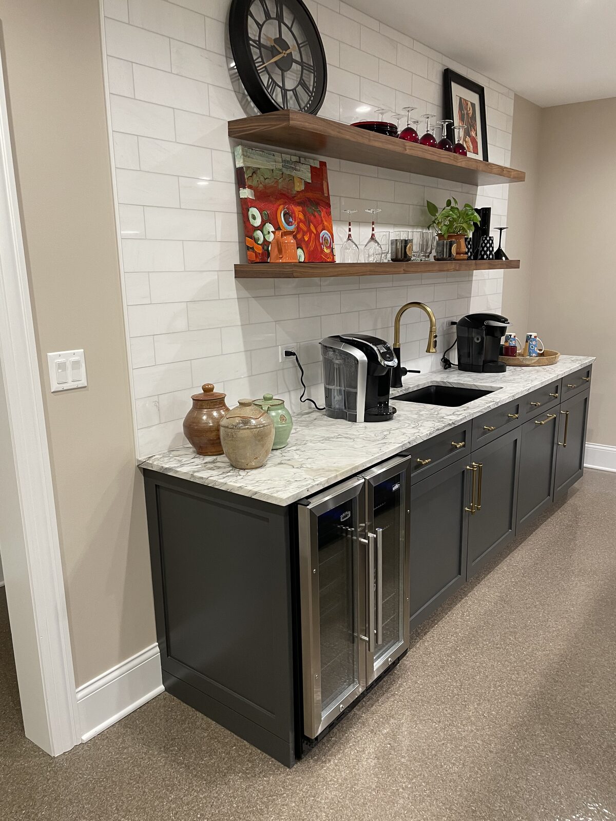 Wet bar wall with charcoal cabinetry, marble backsplash, and walnut floating display shelves