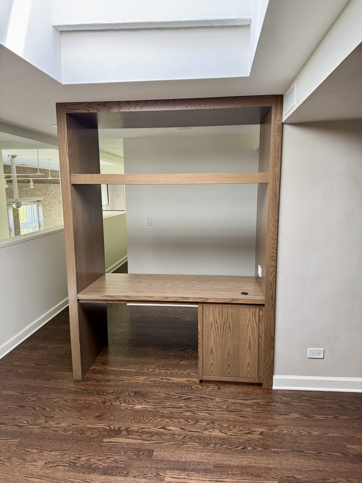 White oak home office built-in with integrated desk niche and natural light from skylight above