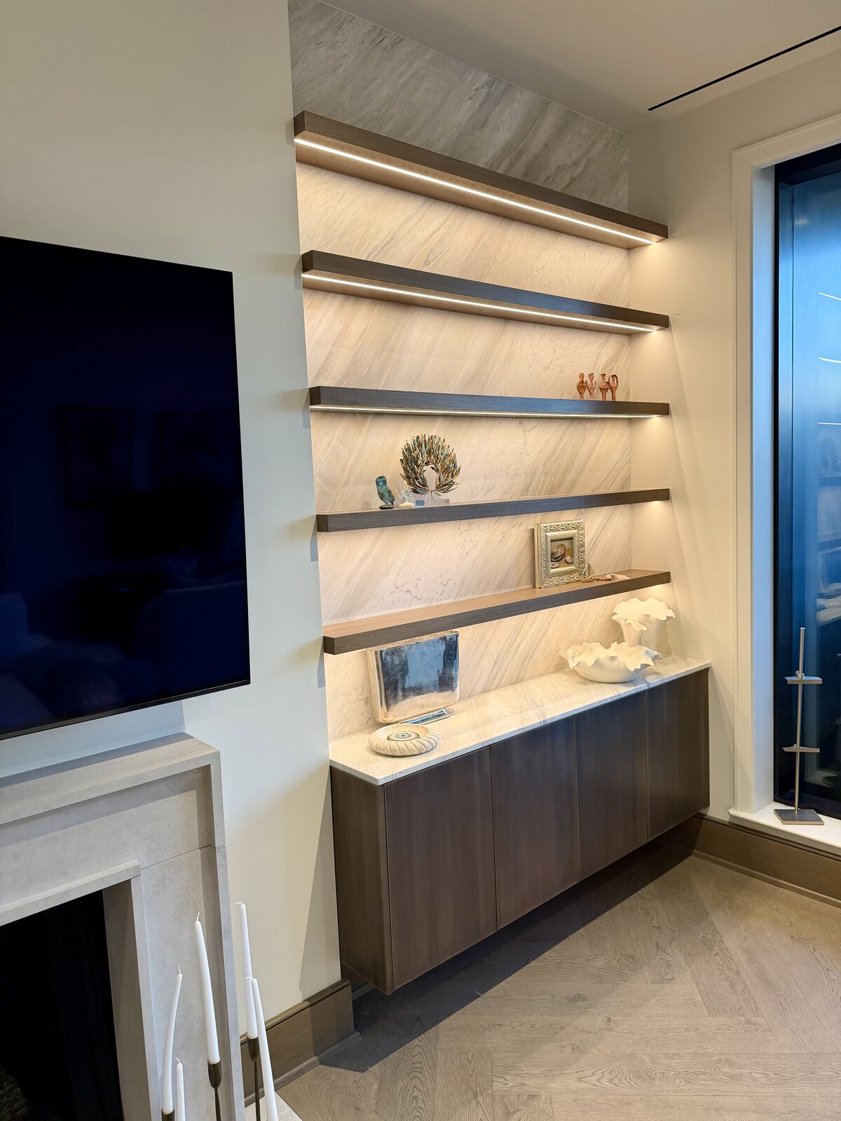 Floating walnut shelf wall with integrated LED lighting and marble slab backing