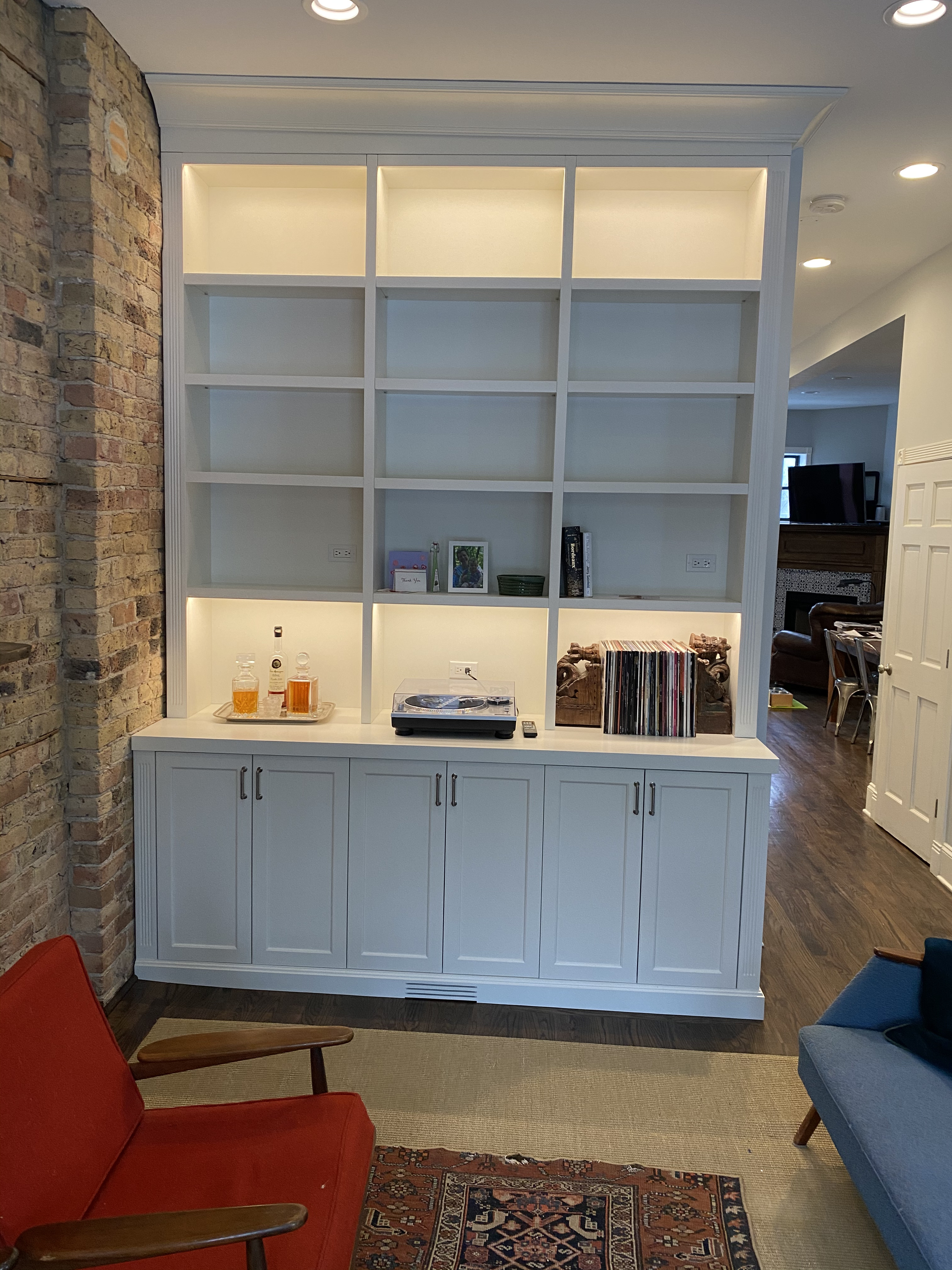 White painted grid-pattern built-in bookshelf with LED lighting and lower shaker cabinet base