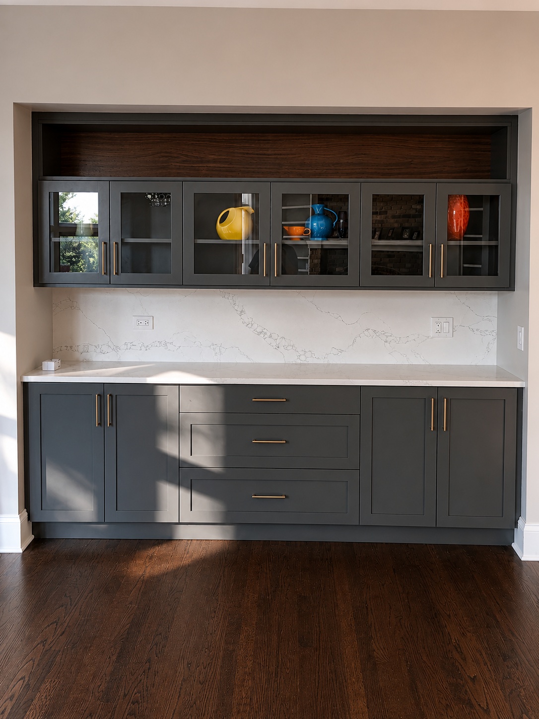 Charcoal painted dining room buffet built-in with glass-front upper display cabinets, marble countertop, and gold bar pulls