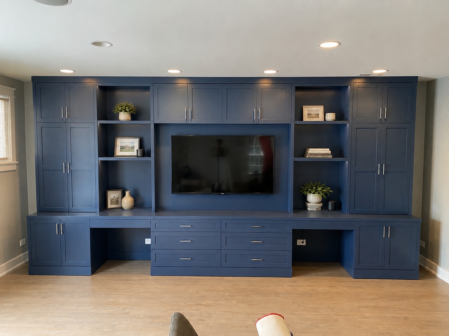 Full-wall navy blue shaker wall unit with TV niche, open display shelving, lower desk surfaces, and tall cabinet towers