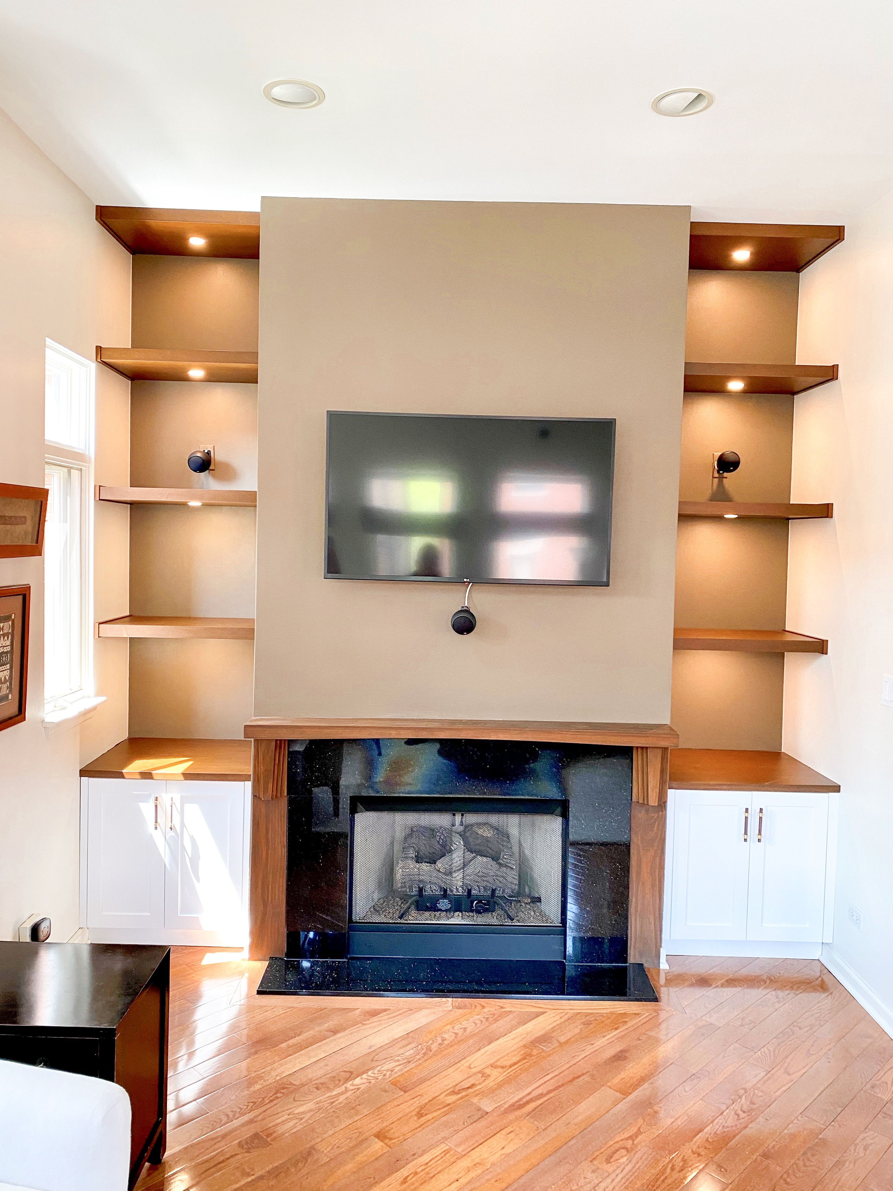 Traditional fireplace wall with warm wood floating shelves, black granite surround, and white lower cabinet storage