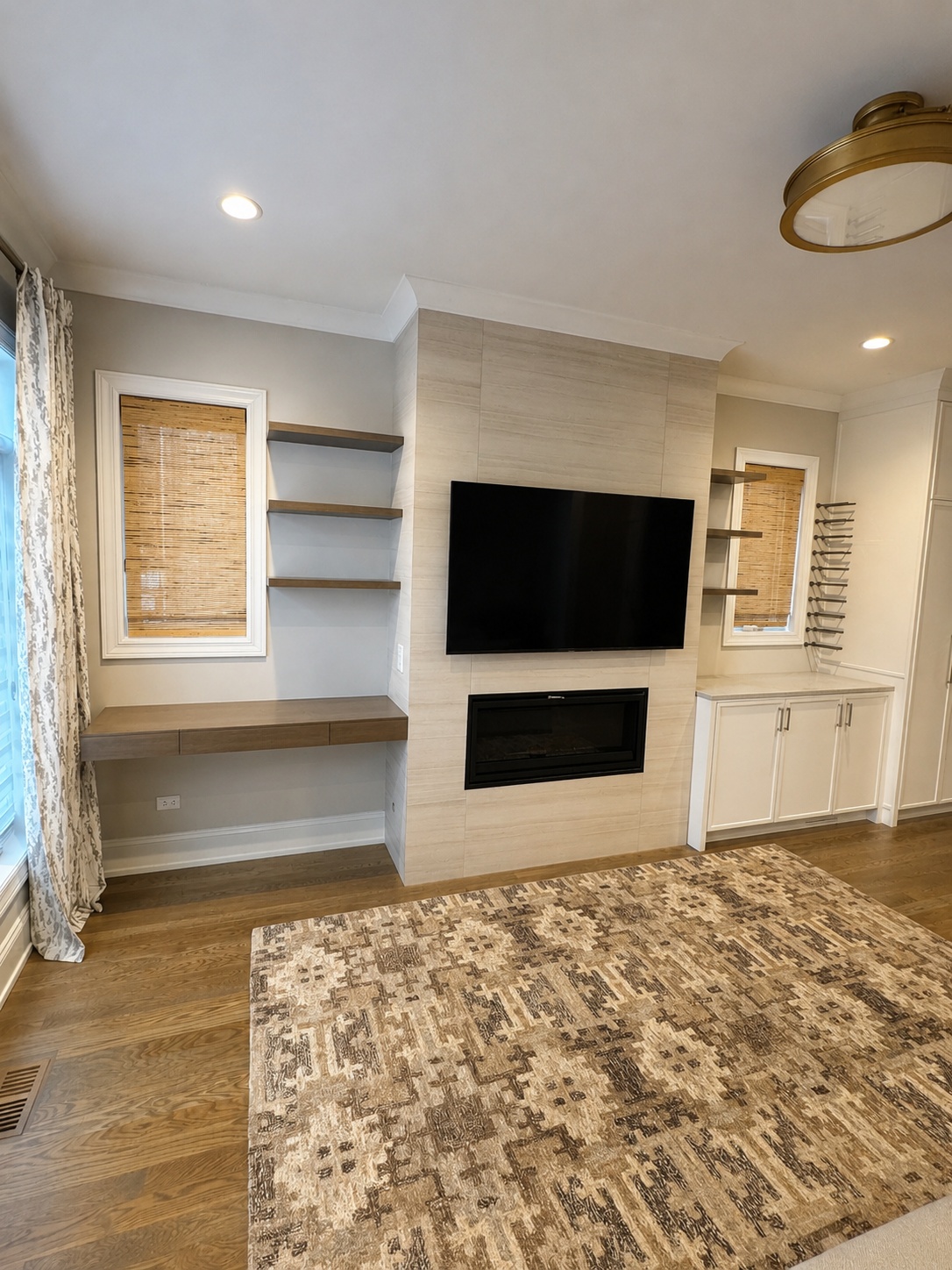 Beige stone tile fireplace wall with TV niche, flanking floating wood shelves, and built-in desk and lower cabinets