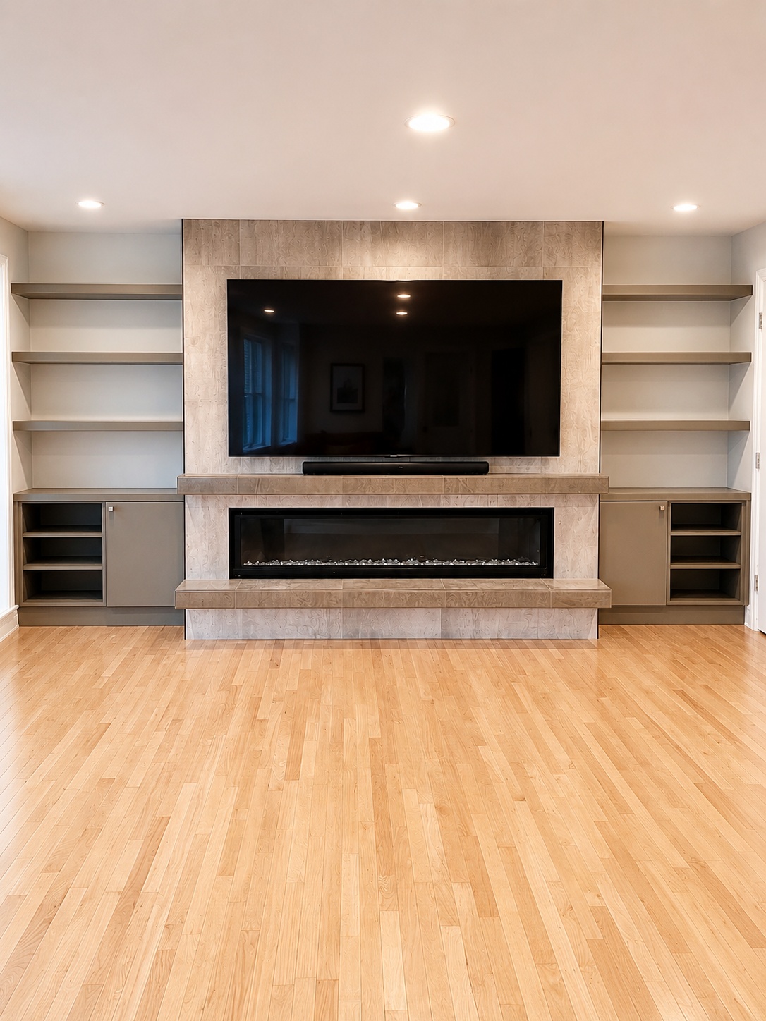 Large modern linear fireplace media wall with stone tile surround, wide-screen TV, and flanking LED floating shelves with lower cabinet storage