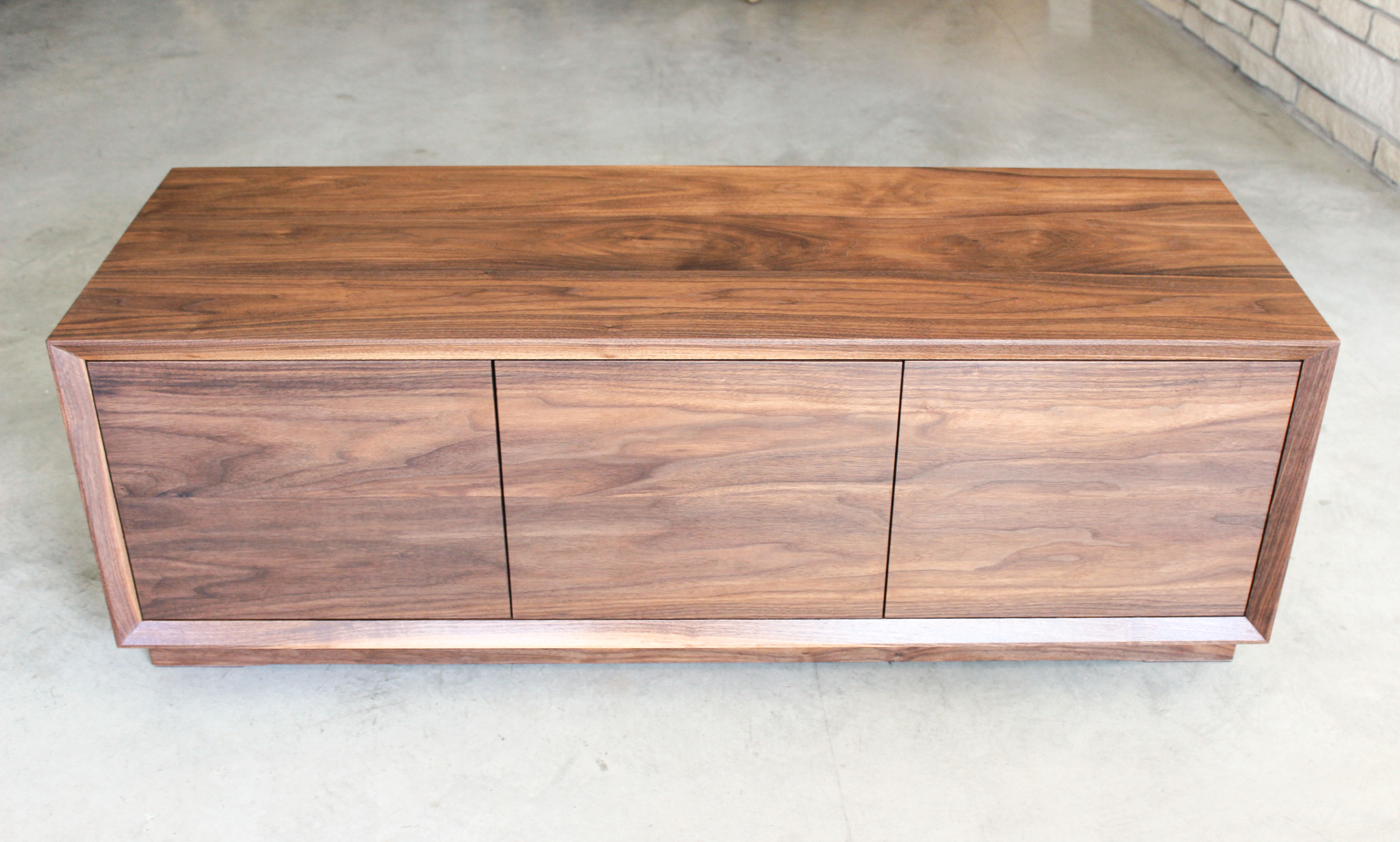 Three-panel walnut credenza built in the New Era Woodworks shop, photographed on polished concrete with brick wall background