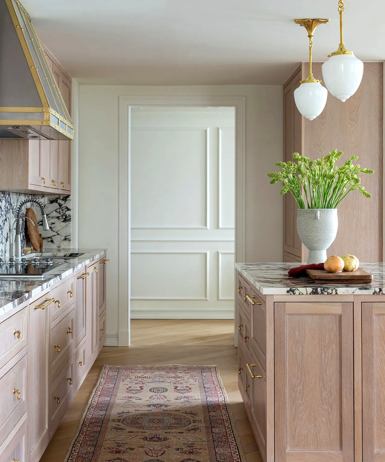 Blush-toned cerused oak galley kitchen with marble slab backsplash and custom steel-and-brass range hood