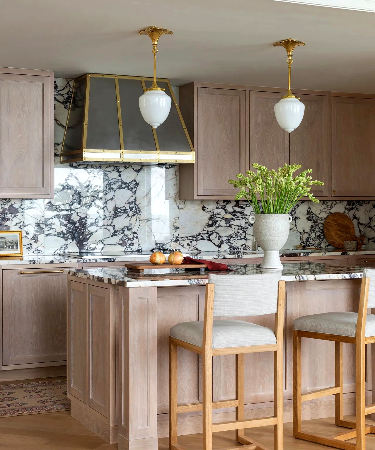 Blush-toned cerused oak kitchen island with full-height marble slab backsplash and custom steel-and-brass range hood