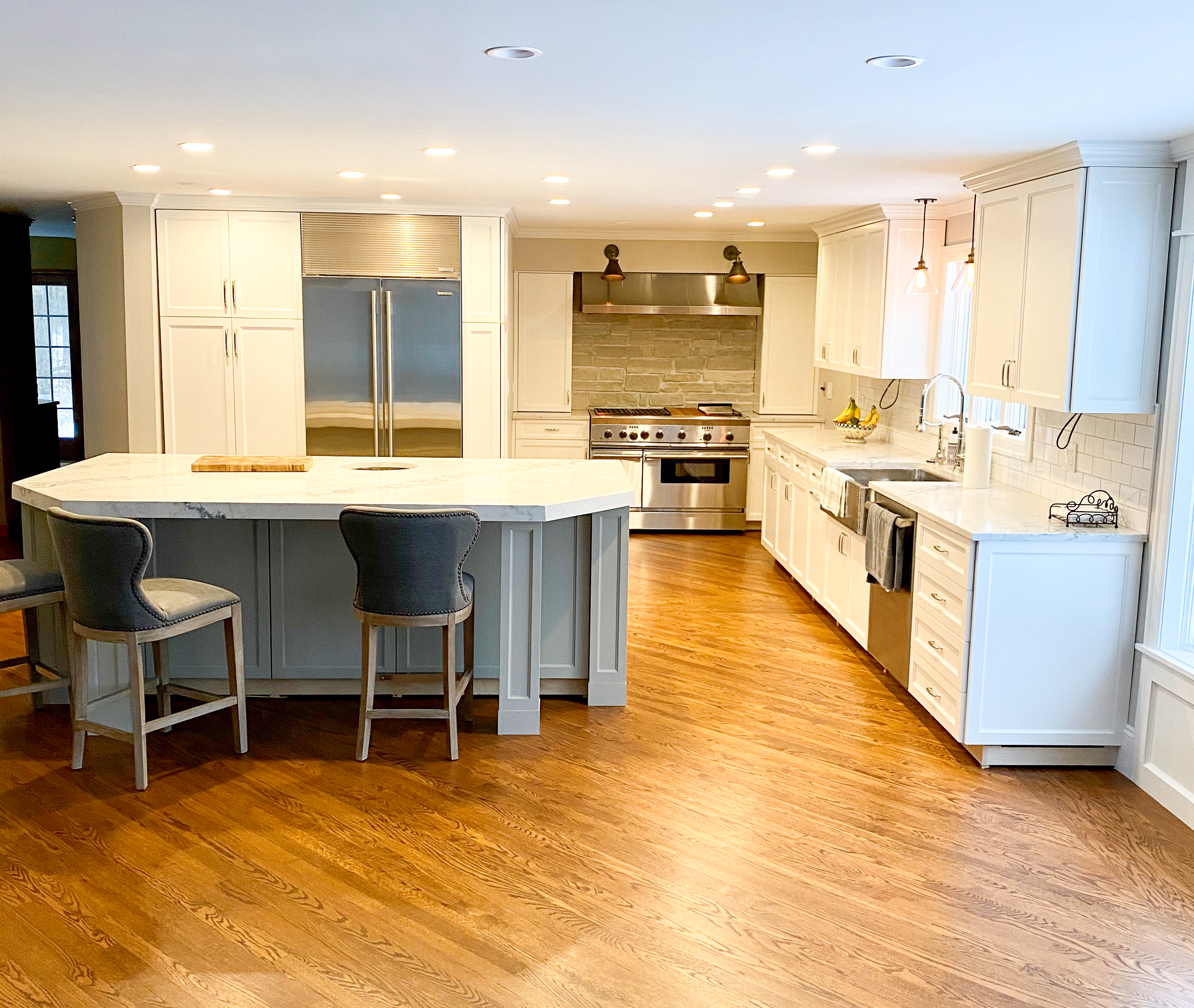 White shaker perimeter kitchen with gray painted island, SubZero refrigerator panel, Wolf range, and farmhouse sink