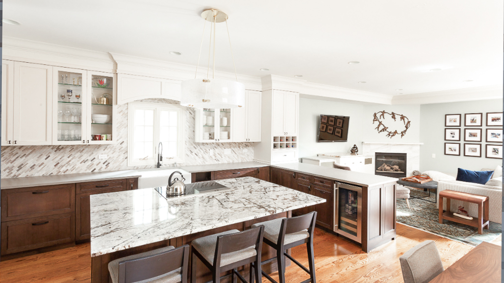 Open-plan kitchen with white upper and espresso lower cabinetry, marble waterfall island, and dining area beyond