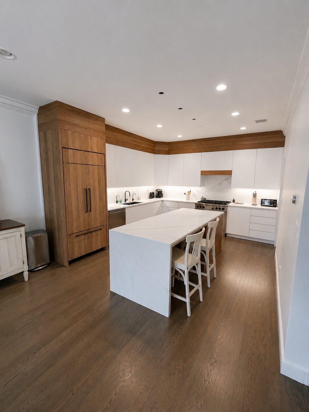 Modern kitchen with natural wood refrigerator tower, white flat-panel cabinetry, and waterfall island