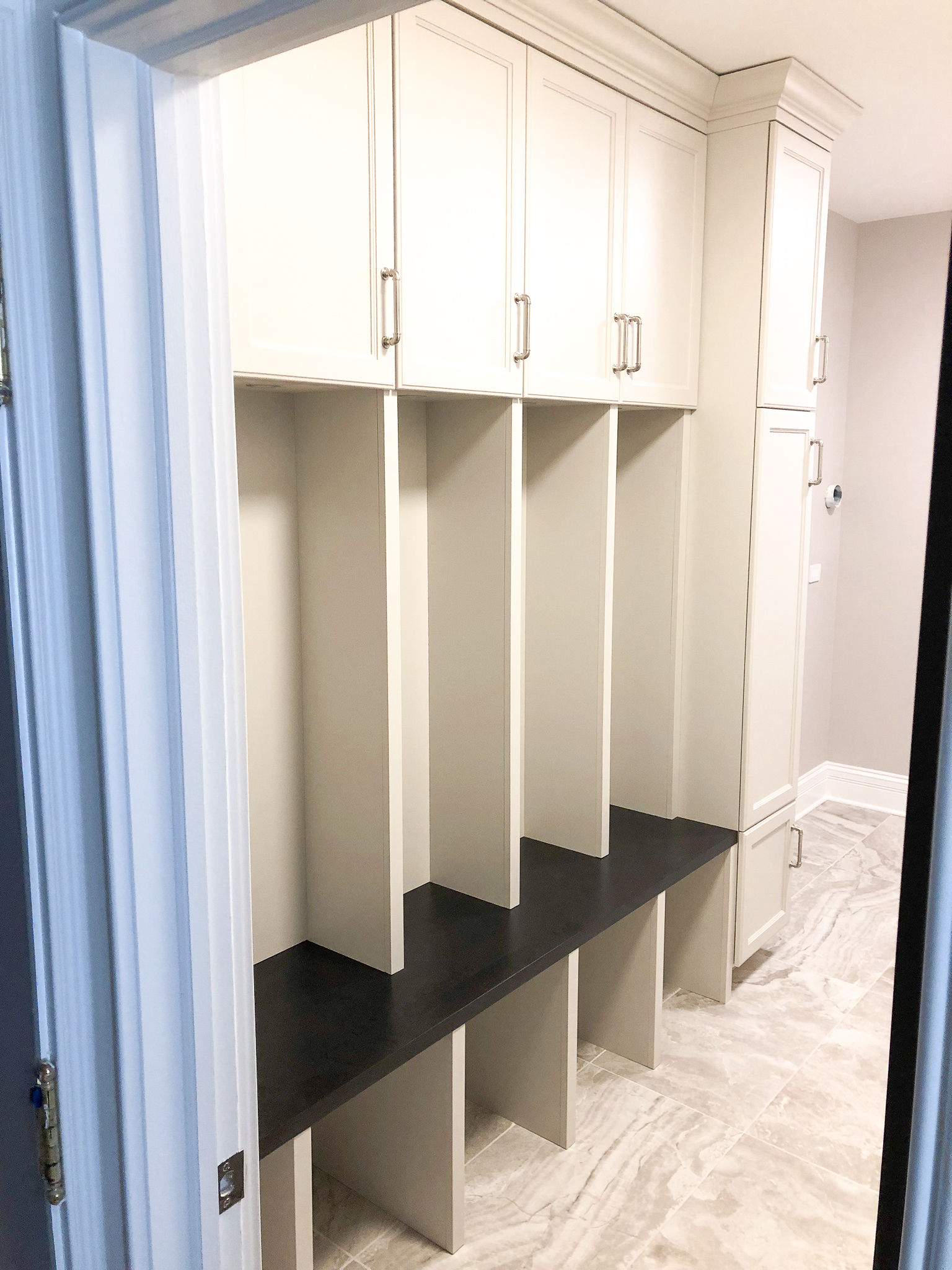 Traditional white painted mudroom with upper cabinets, open cubbies, dark bench top, and marble tile floor