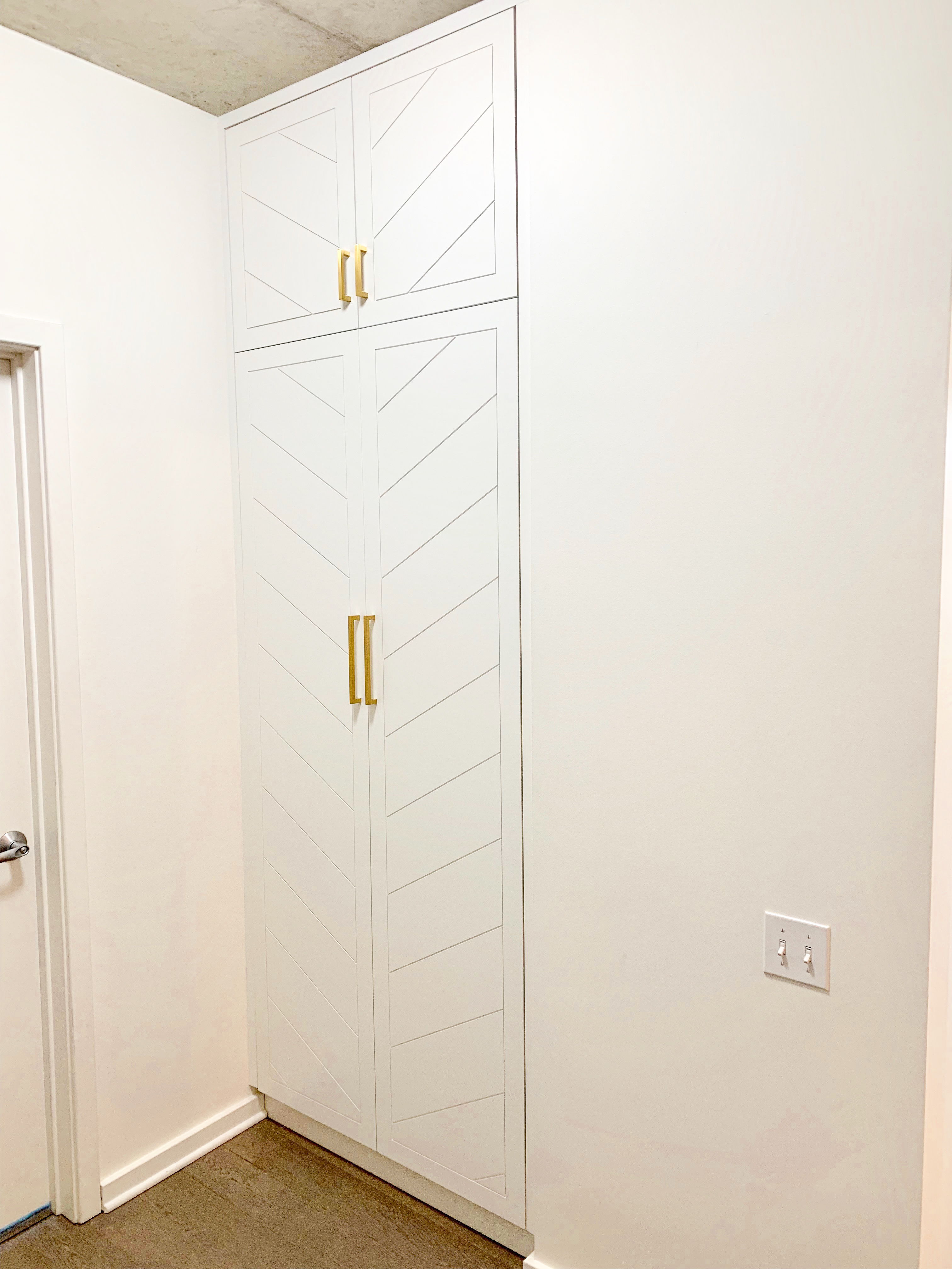 Floor-to-ceiling white painted closet with chevron door pattern and gold bar pulls