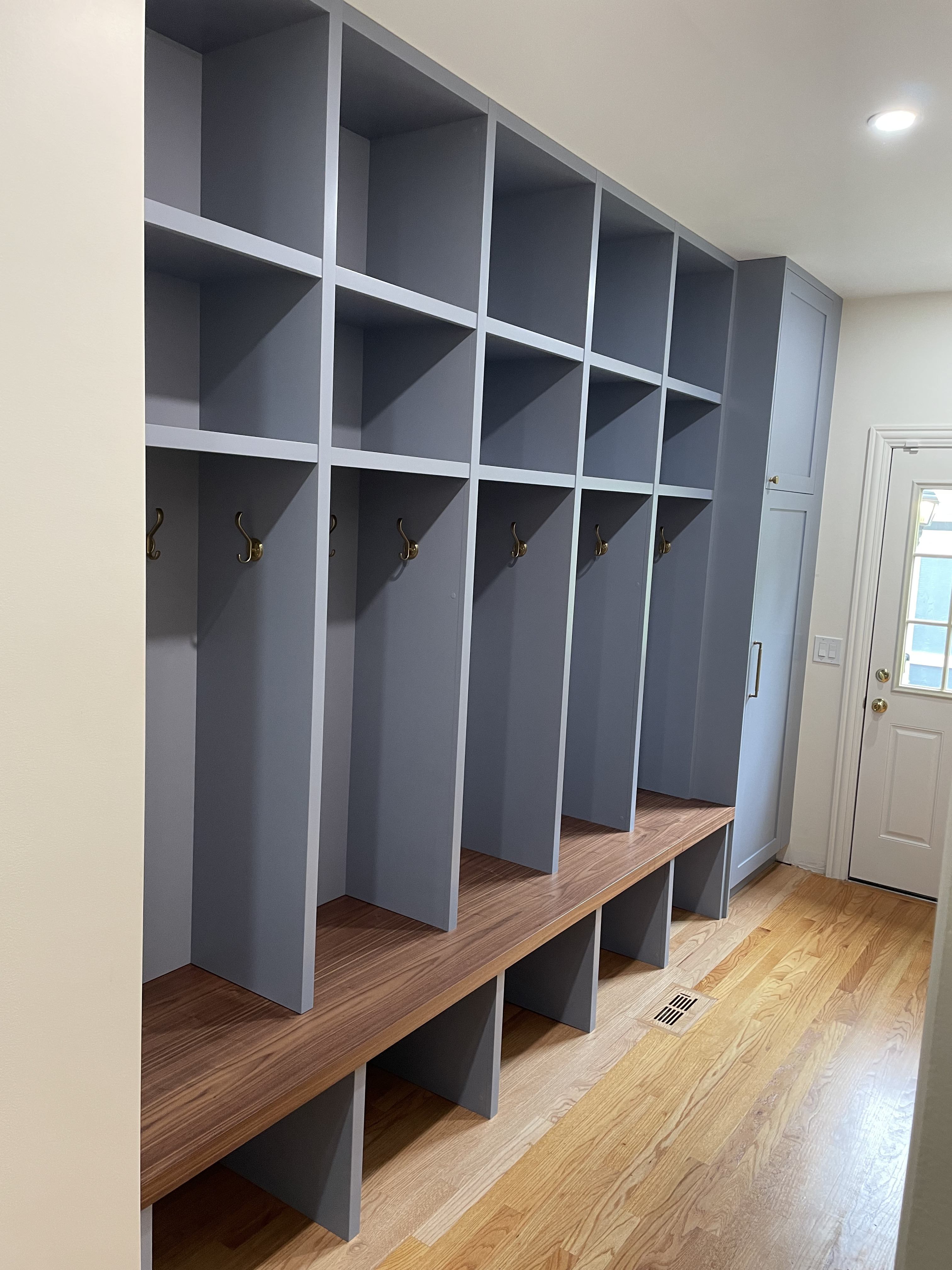 Full-wall slate blue painted mudroom with open locker cubbies, walnut bench, and brass double hooks