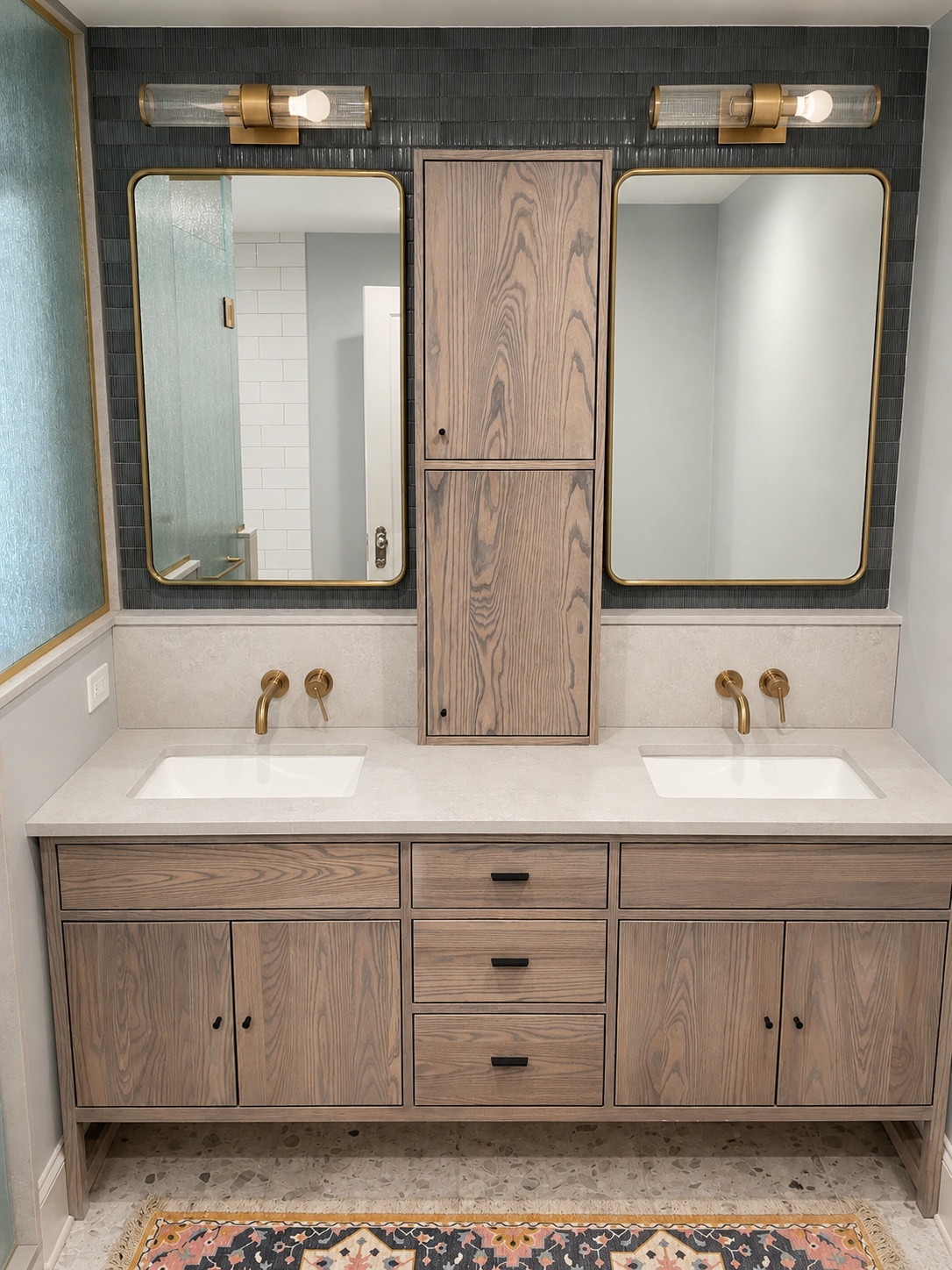 White oak double vanity with brass wall-mount faucets, dark tile backsplash, and center linen tower