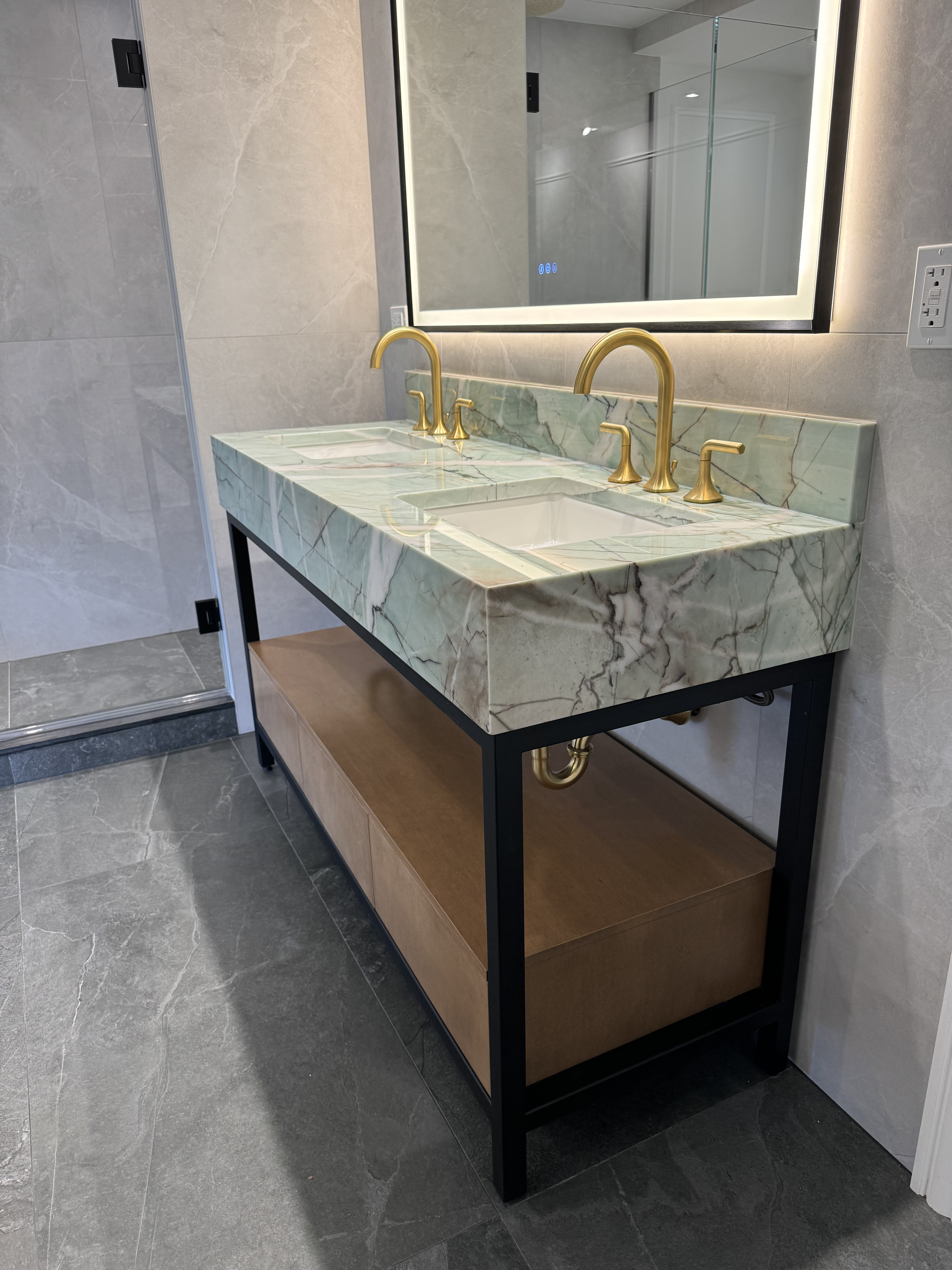 Contemporary double-sink vanity with black steel frame, white oak open shelf, green marble top, and gold faucets